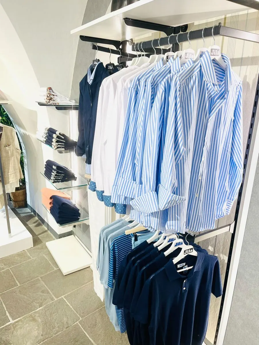 Camicie a righe azzurre e polo esposte su grucce Jila nel negozio di Alassio