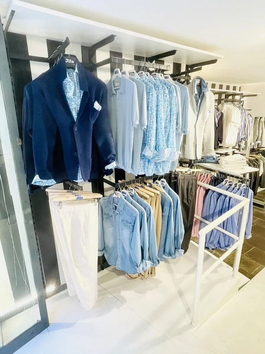 Interno del negozio Jila ad Alassio con blazer navy, camicie e scaffali in esposizione